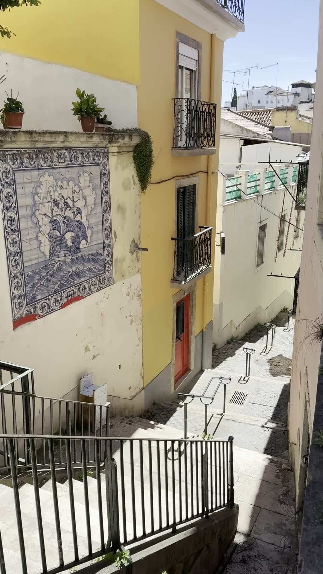 A steep tiled stair street in Alfama with yellow buildings and azulejo tilework.