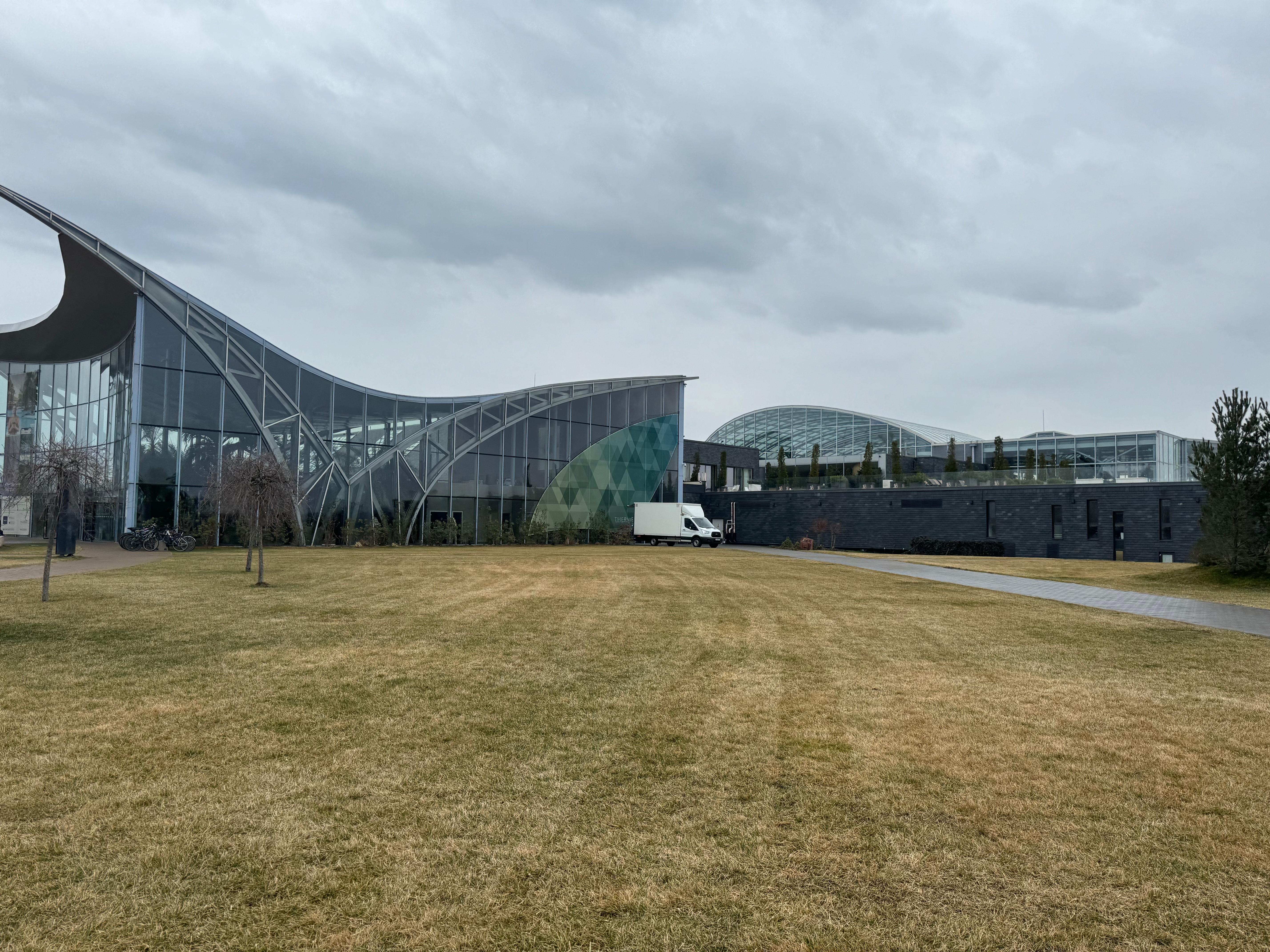 The glass exterior of Therme Bucharest under a cloudy sky