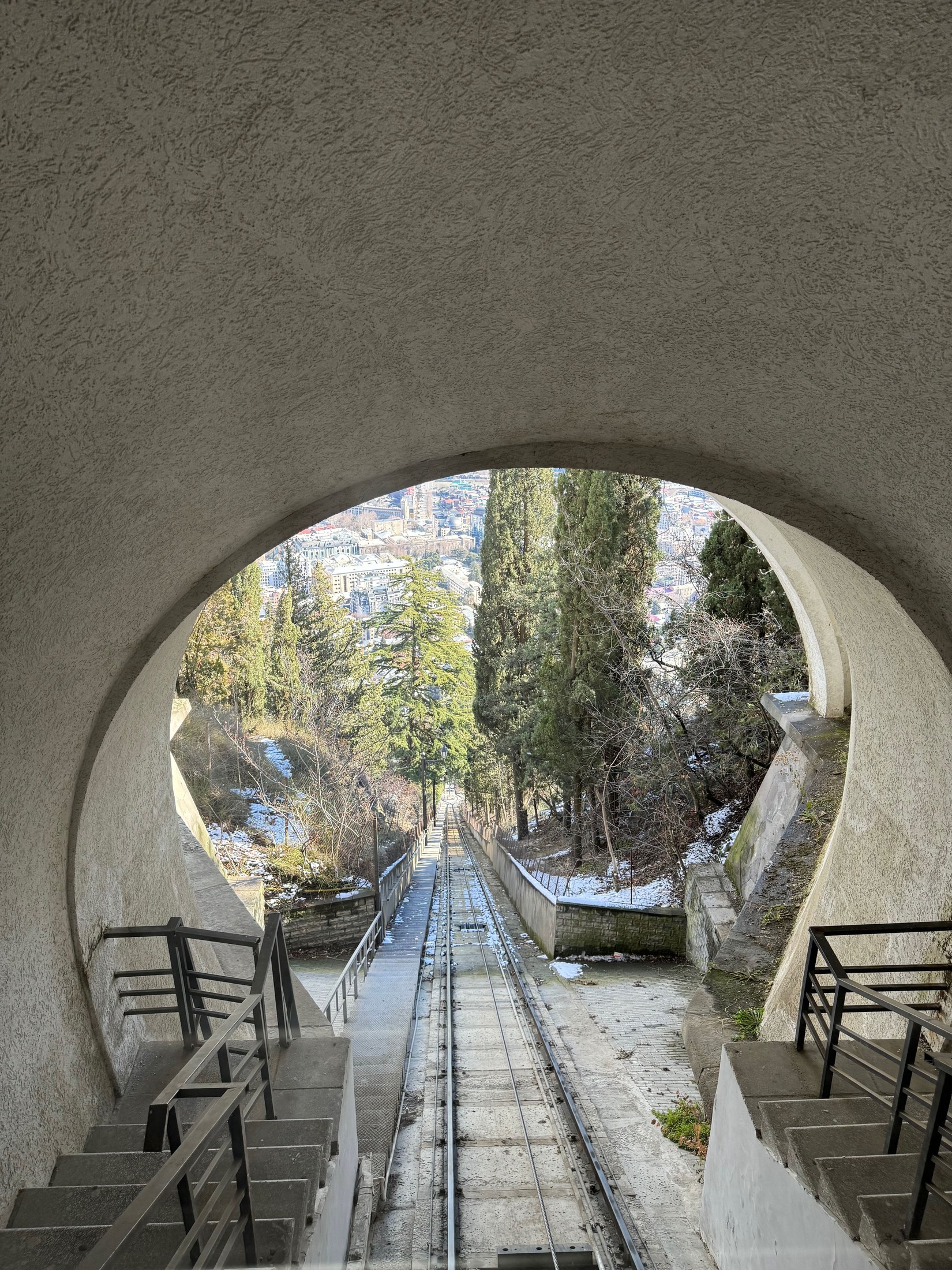 Mtatsminda funicular track descending through an arched station opening above Tbilisi