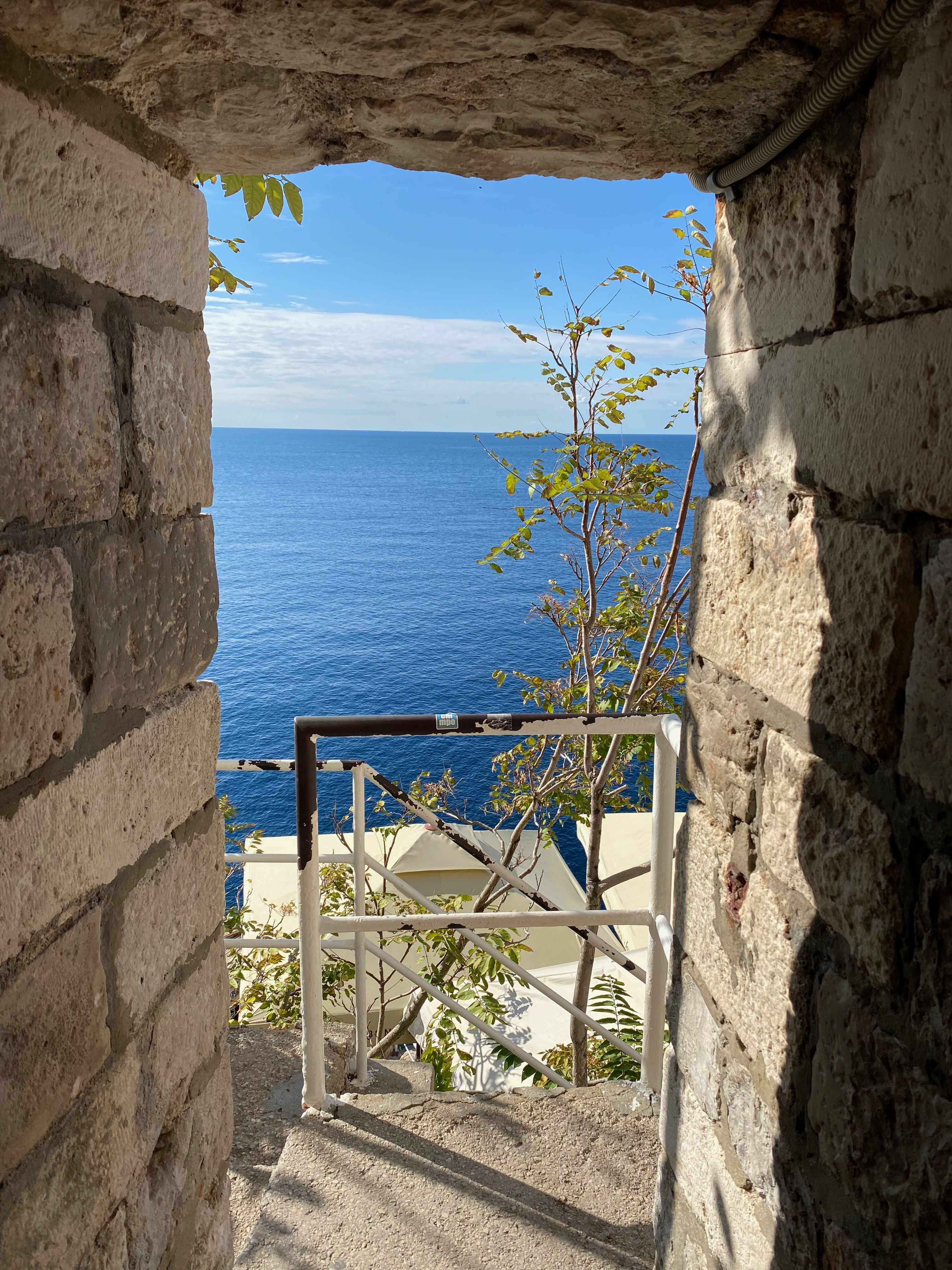 Stone cut-through in the Dubrovnik city walls framing the Adriatic at Buza Bar