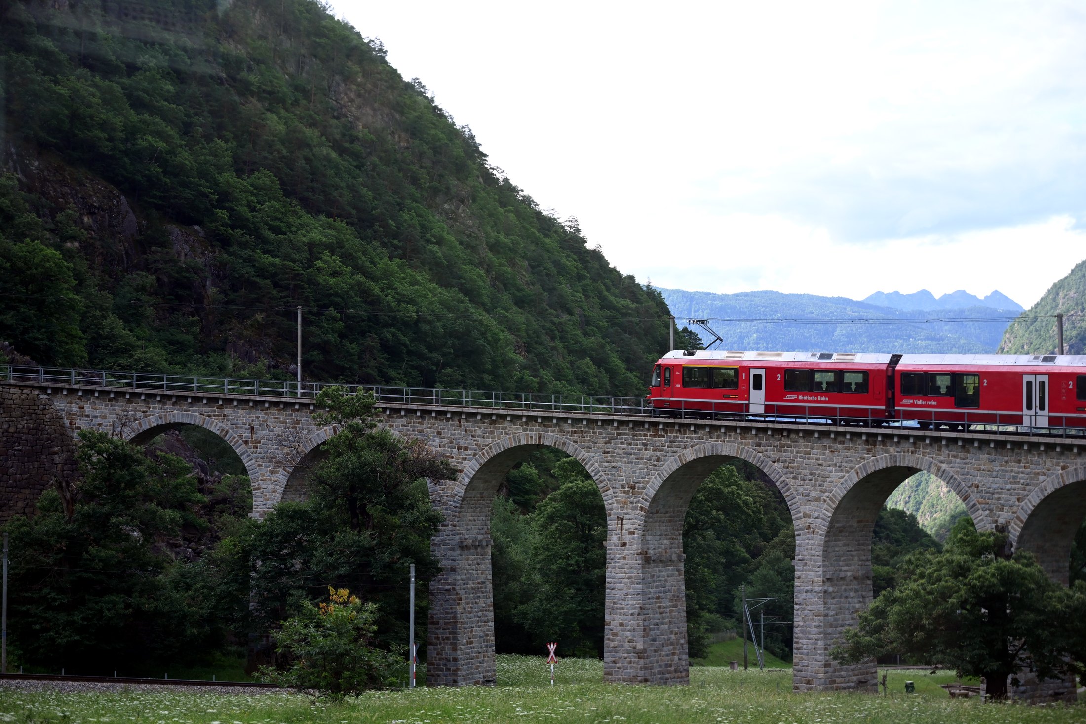 Red RhB train crossing a stone viaduct on the Bernina route